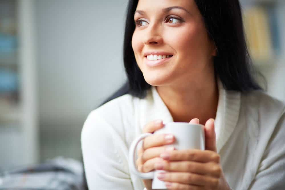 A woman holding a cup of coffee and smiling - showing the effects of coffee on teeth.