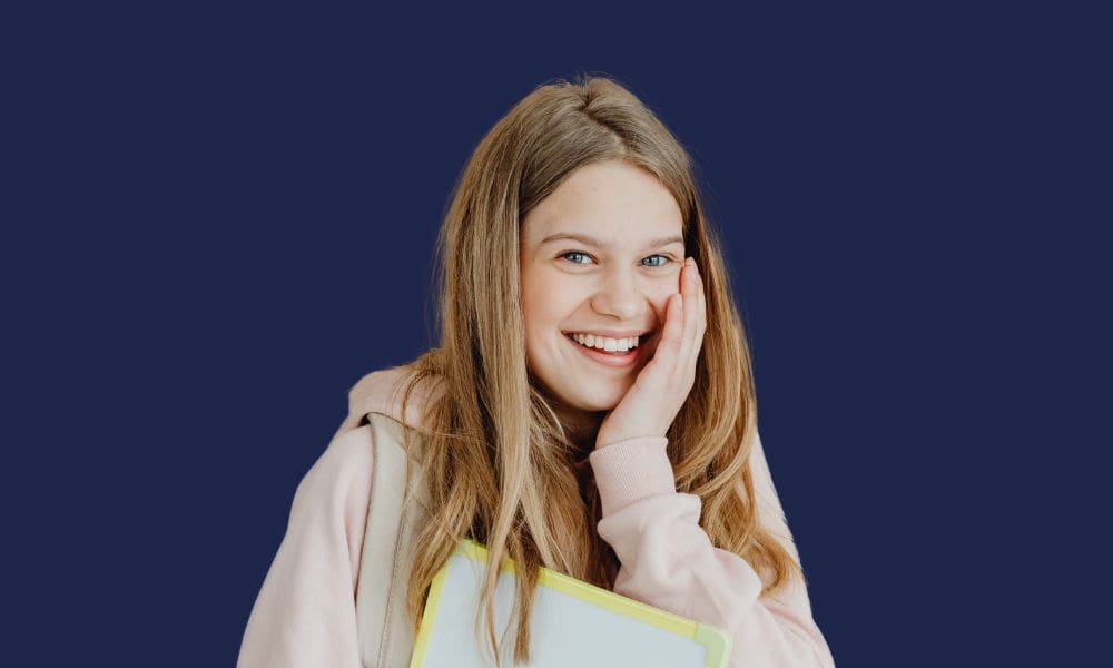 A young woman smiling confidently, showcasing early signs of gum recession, against a navy background.