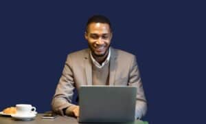 Indoda egqoke ibhulashi elinsundu iyamomotheka ngenkathi isebenza kwi-laptop yayo edeskini elinekhofi namakhekhe.