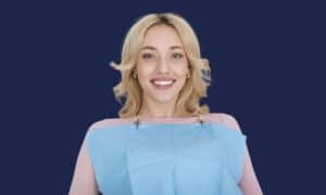 Une femme, souriante et confiante, est assise sur un fauteuil dentaire et porte un bavoir au cabinet dentaire OptiSmile du Cap.