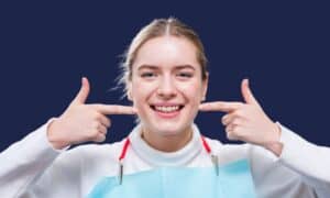 Una joven señala su sonrisa durante una revisión dental, comprendiendo qué cubre el seguro médico para el tratamiento dental.
