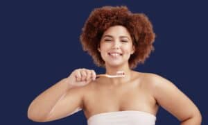 Woman smiling while brushing her teeth correctly with the right brushing technique to protect enamel and gums