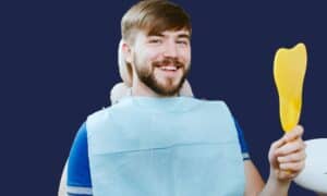 Smiling dental patient holding a mirror illustrating the difference between a general dentist and a specialist.