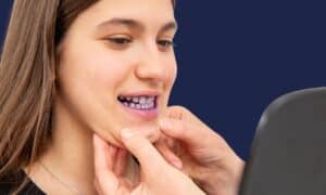 A smiling woman in a mirror shows a plaque stained pink and purple by a disclosing tablet along her gum line.