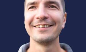 Smiling man against a navy background, with one upper front tooth noticeably darker than the teeth beside it.