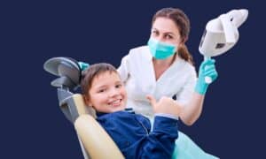 A happy child giving a thumbs up in the dentist's chair at a children's dental check-up.