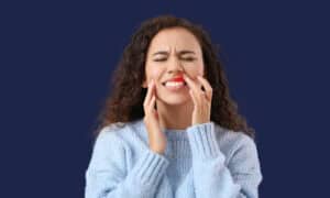 Woman with her eyes shut in discomfort, holding her jaw, with inflamed red gums highlighted