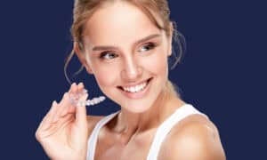 Smiling woman holding a clear dental aligner, the type of treatment that can be monitored from home by phone