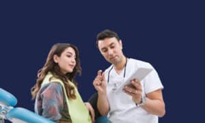 Dentist showing a patient her treatment plan on a tablet while she sits in the dental chair.